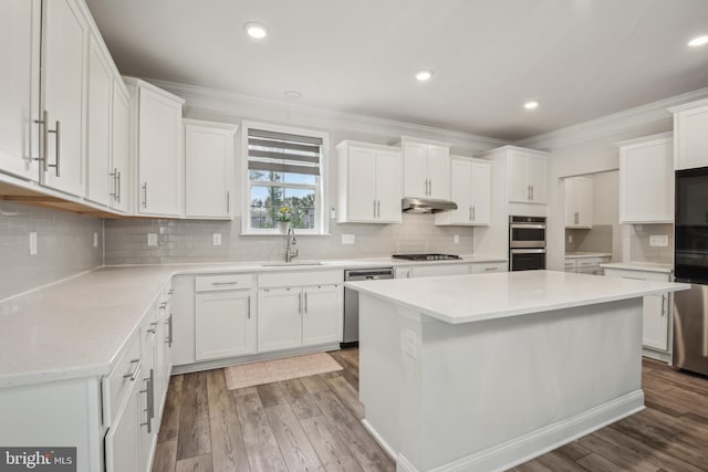 kitchen with a sink, under cabinet range hood, white cabinetry, backsplash, and appliances with stainless steel finishes