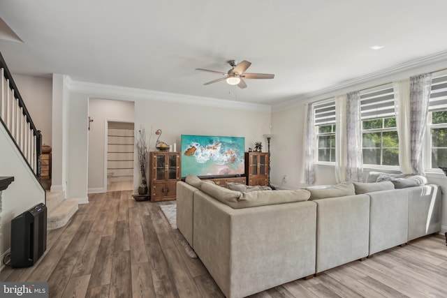 living area featuring wood finished floors, baseboards, ceiling fan, ornamental molding, and stairs