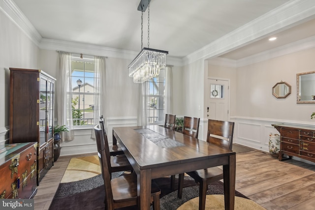dining room featuring an inviting chandelier, wood finished floors, a wainscoted wall, a decorative wall, and ornamental molding