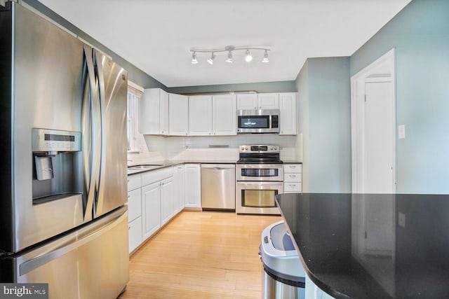 kitchen featuring appliances with stainless steel finishes, light wood finished floors, white cabinetry, and backsplash