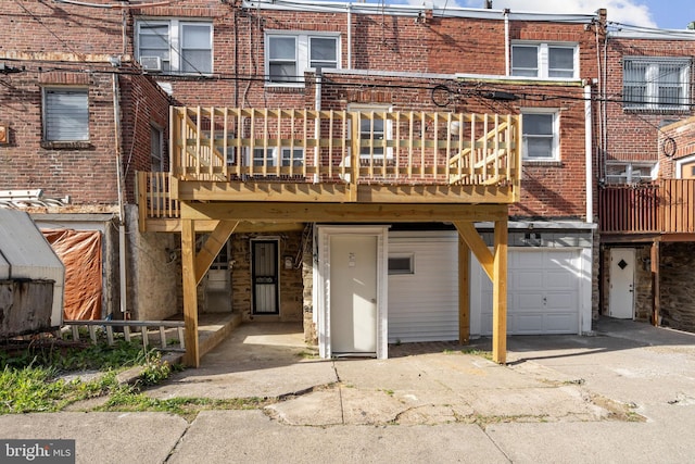 rear view of house with a wooden deck, an attached garage, brick siding, and driveway