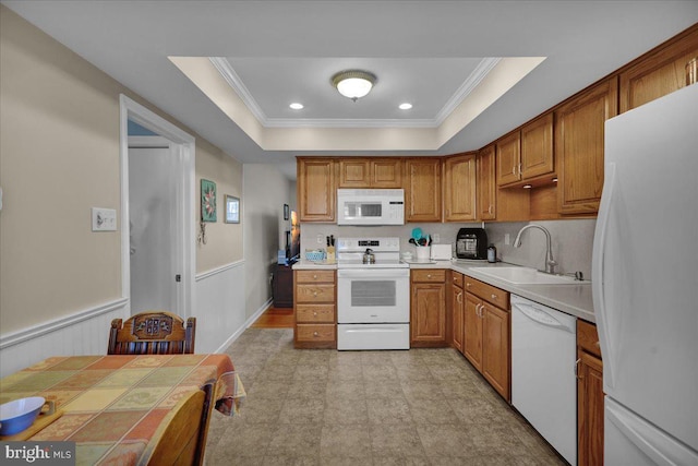 kitchen with white appliances, a sink, brown cabinets, crown molding, and a raised ceiling