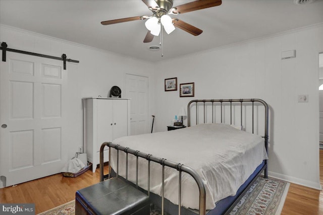 bedroom featuring a ceiling fan, crown molding, light wood finished floors, and a barn door