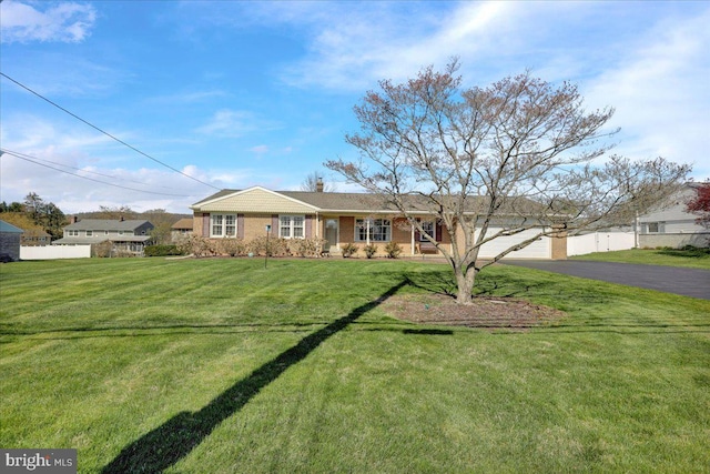 ranch-style house featuring a front yard, brick siding, fence, and aphalt driveway