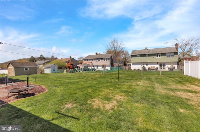 view of yard with fence, an outdoor structure, a residential view, a fire pit, and a playground