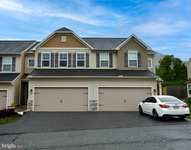 view of front of house with an attached garage, asphalt driveway, roof with shingles, and stone siding
