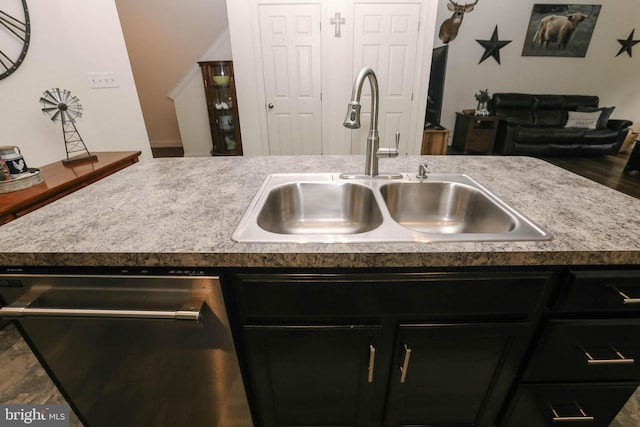 kitchen featuring stainless steel dishwasher, a sink, dark cabinets, open floor plan, and vaulted ceiling