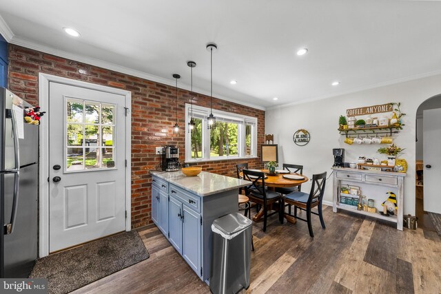 kitchen with freestanding refrigerator, healthy amount of natural light, blue cabinetry, dark wood finished floors, and brick wall