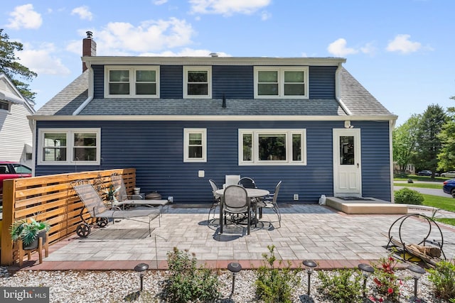 back of property with roof with shingles, a chimney, and a patio
