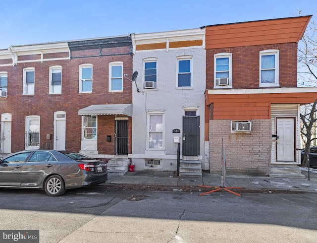 view of property featuring entry steps, cooling unit, brick siding, and a wall mounted AC