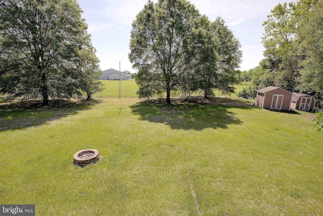 view of grassy yard with a storage unit, an outbuilding, and an outdoor fire pit