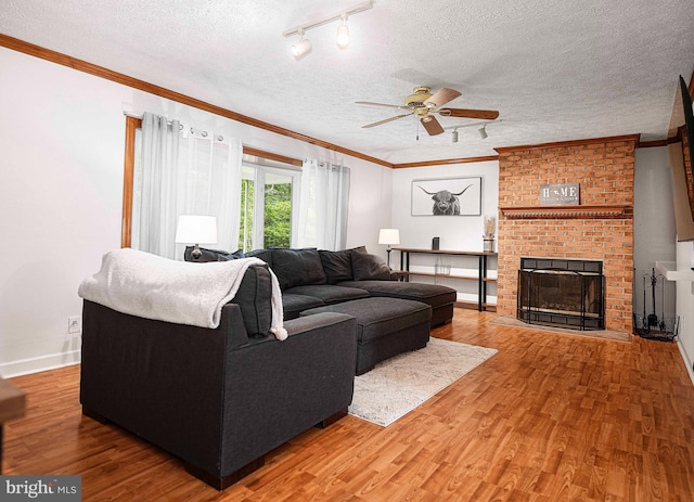 living area featuring a textured ceiling, wood finished floors, a ceiling fan, a fireplace, and crown molding