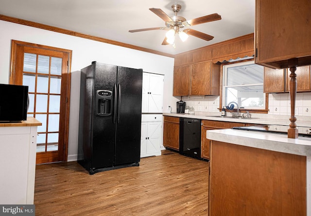 kitchen featuring black appliances, a sink, crown molding, light wood-type flooring, and brown cabinets