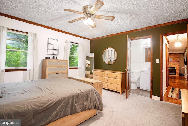 bedroom with light colored carpet, a textured ceiling, ornamental molding, a large fireplace, and ensuite bath