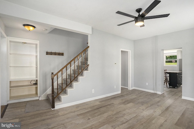 unfurnished living room featuring wood finished floors, stairway, a ceiling fan, and baseboards