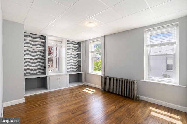 unfurnished room featuring radiator heating unit, wood finished floors, baseboards, and a drop ceiling