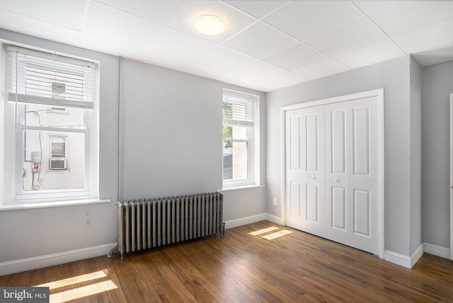 unfurnished bedroom with radiator, baseboards, wood finished floors, a closet, and a drop ceiling