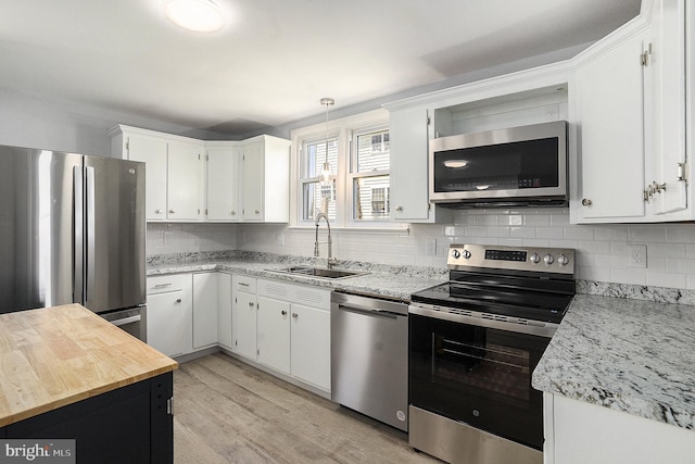 kitchen featuring appliances with stainless steel finishes, a sink, backsplash, white cabinets, and light wood finished floors