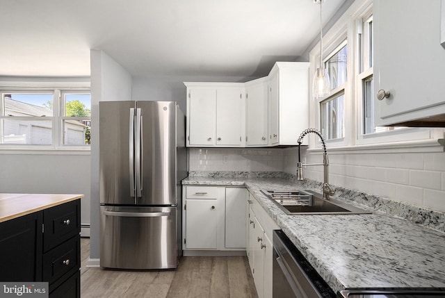 kitchen with appliances with stainless steel finishes, a sink, light wood-style flooring, white cabinets, and decorative backsplash
