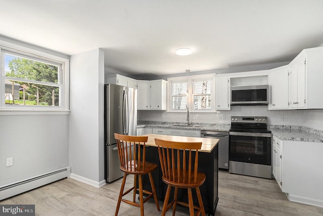 kitchen featuring stainless steel appliances, a baseboard radiator, decorative backsplash, and light wood finished floors