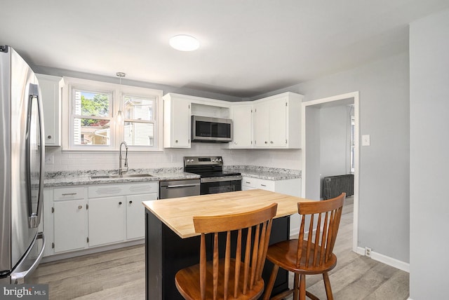 kitchen with stainless steel appliances, a sink, decorative backsplash, light wood finished floors, and white cabinets
