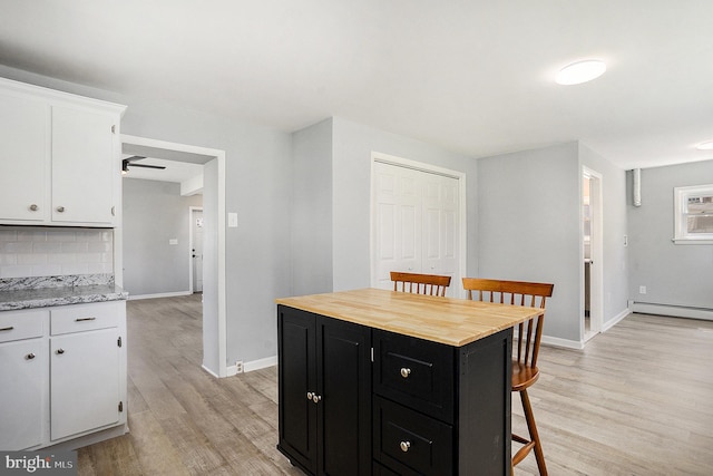 kitchen featuring dark cabinetry, light wood-style flooring, white cabinets, a kitchen breakfast bar, and backsplash