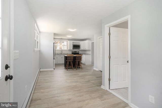 hall with light wood finished floors, baseboard heating, baseboards, and a sink