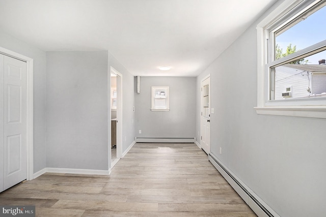hallway featuring a baseboard heating unit, a baseboard radiator, healthy amount of natural light, and light wood-type flooring