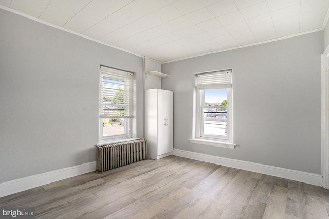 unfurnished room featuring radiator, crown molding, light wood-type flooring, and baseboards