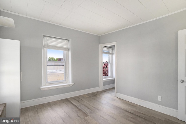 empty room featuring crown molding, plenty of natural light, wood finished floors, and baseboards