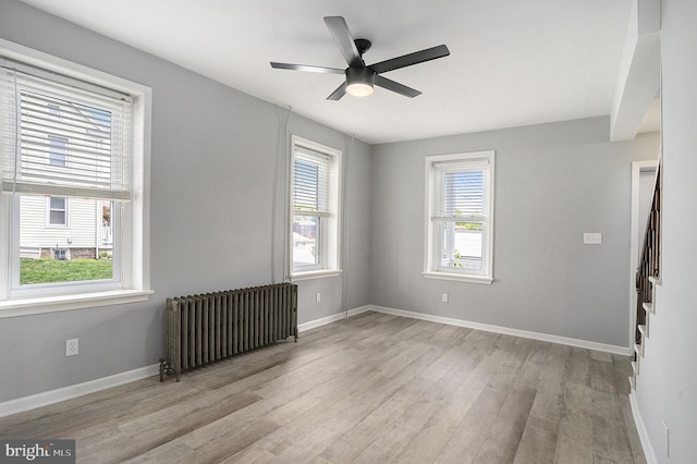 unfurnished room featuring radiator, wood finished floors, stairs, a ceiling fan, and baseboards