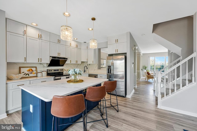 kitchen featuring a center island, light wood-style floors, stainless steel appliances, and light stone countertops