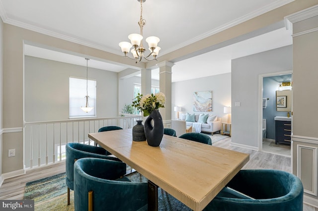 dining room featuring a chandelier, light wood-style flooring, crown molding, and decorative columns