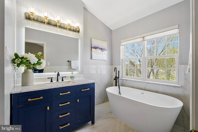 bathroom featuring tile walls, marble finish floor, vanity, a soaking tub, and vaulted ceiling