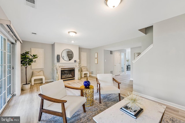 living room featuring baseboards, a high end fireplace, visible vents, and wood finished floors