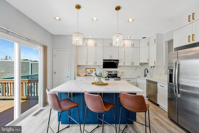 kitchen featuring a center island, a sink, stainless steel appliances, light wood-type flooring, and backsplash
