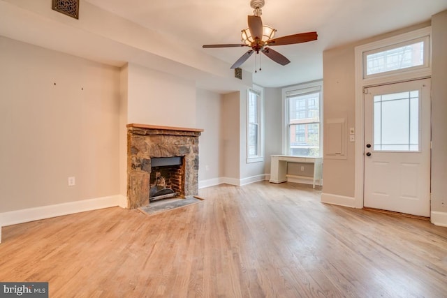 unfurnished living room with visible vents, wood finished floors, baseboards, and a stone fireplace