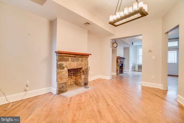 unfurnished living room with visible vents, wood finished floors, baseboards, and a stone fireplace