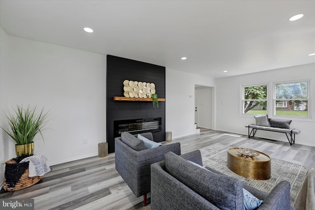 living area featuring light wood-type flooring, a fireplace, recessed lighting, and baseboards