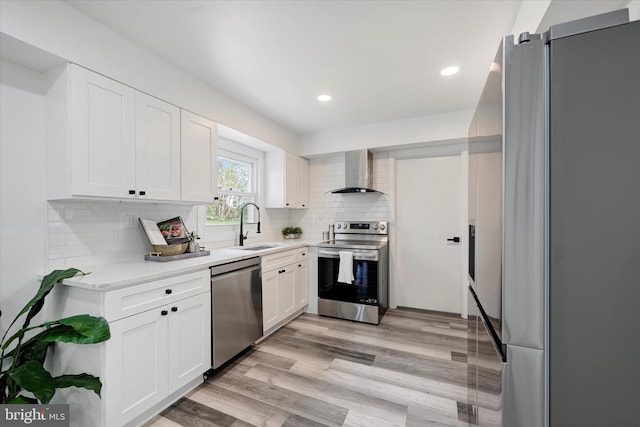 kitchen with appliances with stainless steel finishes, wall chimney range hood, a sink, light countertops, and white cabinets