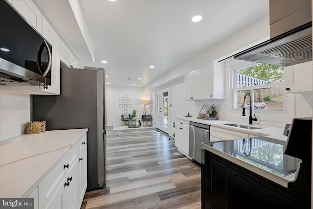 kitchen with appliances with stainless steel finishes, a sink, backsplash, light wood finished floors, and extractor fan