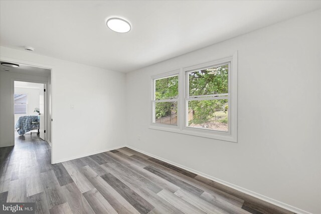 empty room with wood finished floors, a smoke detector, and baseboards