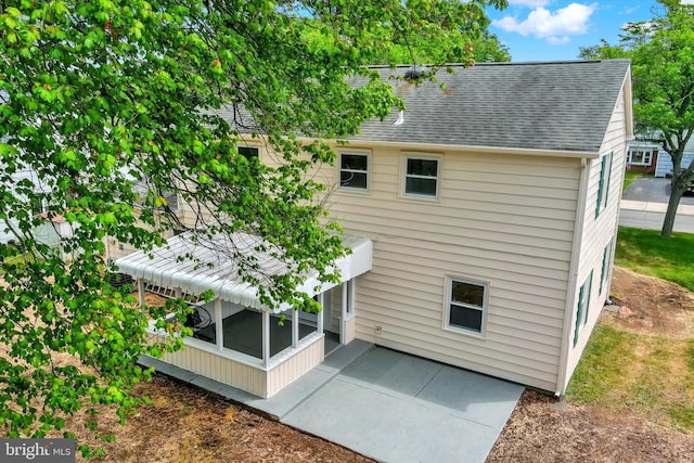 back of house featuring roof with shingles, a sunroom, and a patio