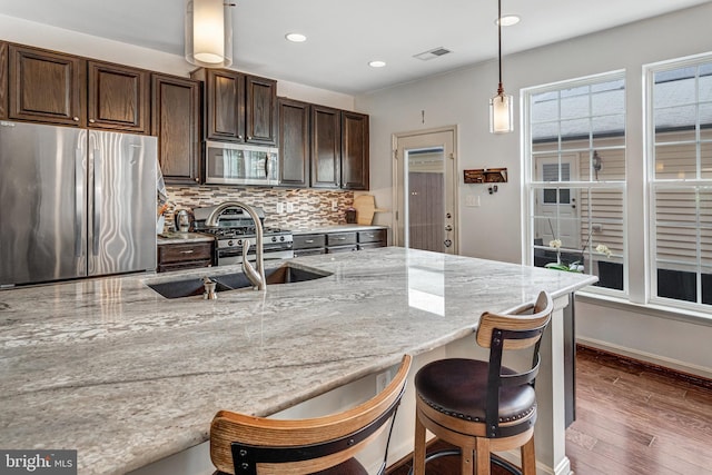 11972 Tygart Lake Dr, Bristow, VA 20136 - kitchen with stainless steel appliances, wood finished floors, backsplash, dark brown cabinetry, and light stone counters
