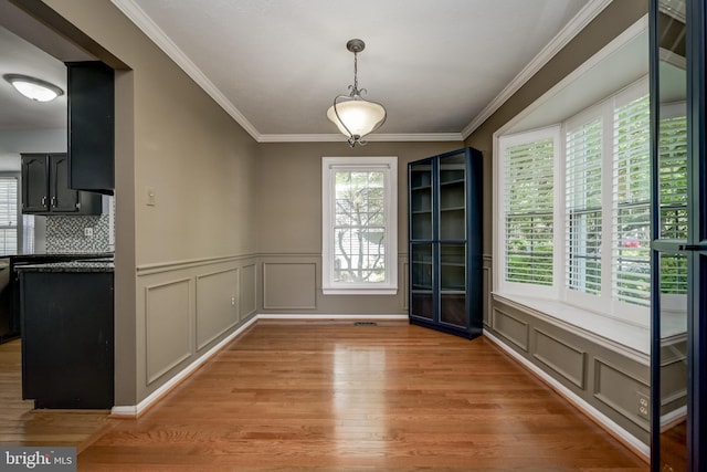 unfurnished dining area with light wood-style flooring, ornamental molding, a decorative wall, and wainscoting