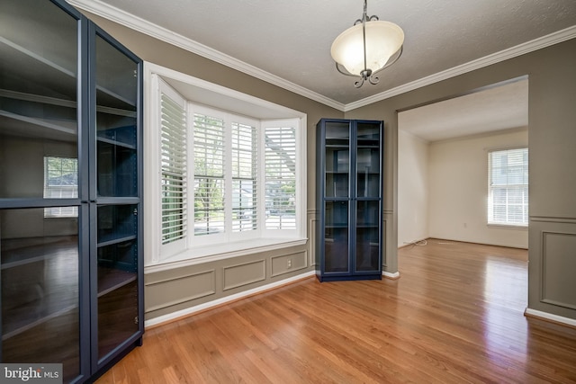 unfurnished dining area with wood finished floors, ornamental molding, and a decorative wall