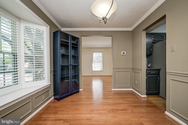 unfurnished dining area featuring a decorative wall, light wood-style floors, ornamental molding, and wainscoting
