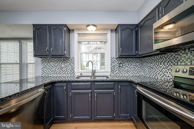 kitchen featuring appliances with stainless steel finishes, a sink, dark stone counters, tasteful backsplash, and light wood-style flooring