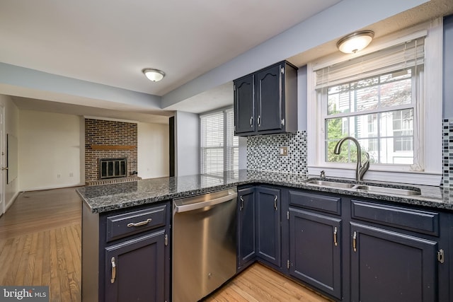kitchen with stainless steel dishwasher, a sink, a peninsula, decorative backsplash, and dark stone countertops