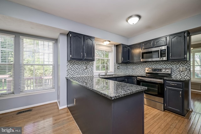 kitchen featuring stainless steel appliances, light wood-style flooring, dark stone counters, baseboards, and decorative backsplash